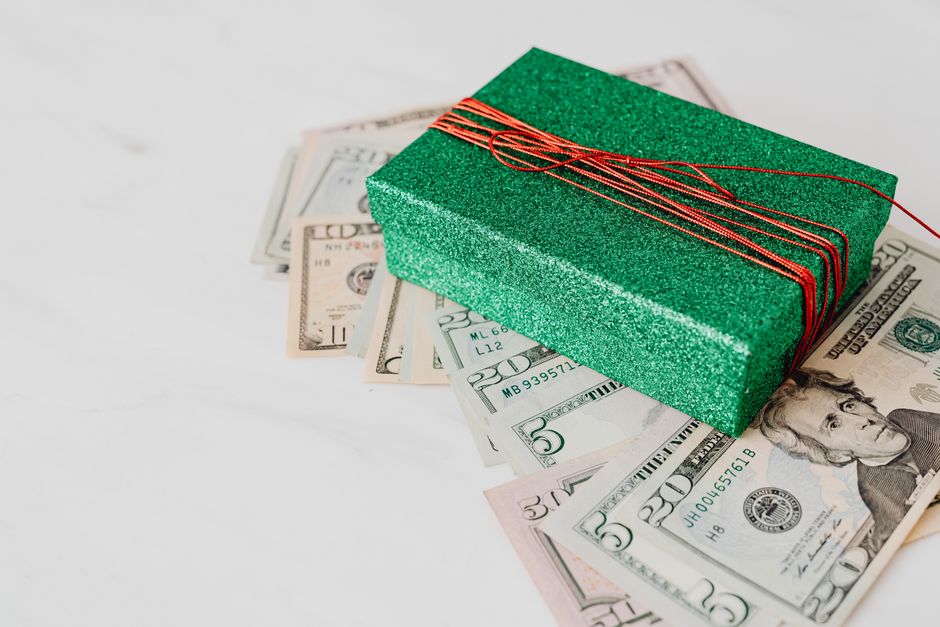 A sparkling green gift box sits atop scattered US dollar bills, emphasizing wealth and generosity.